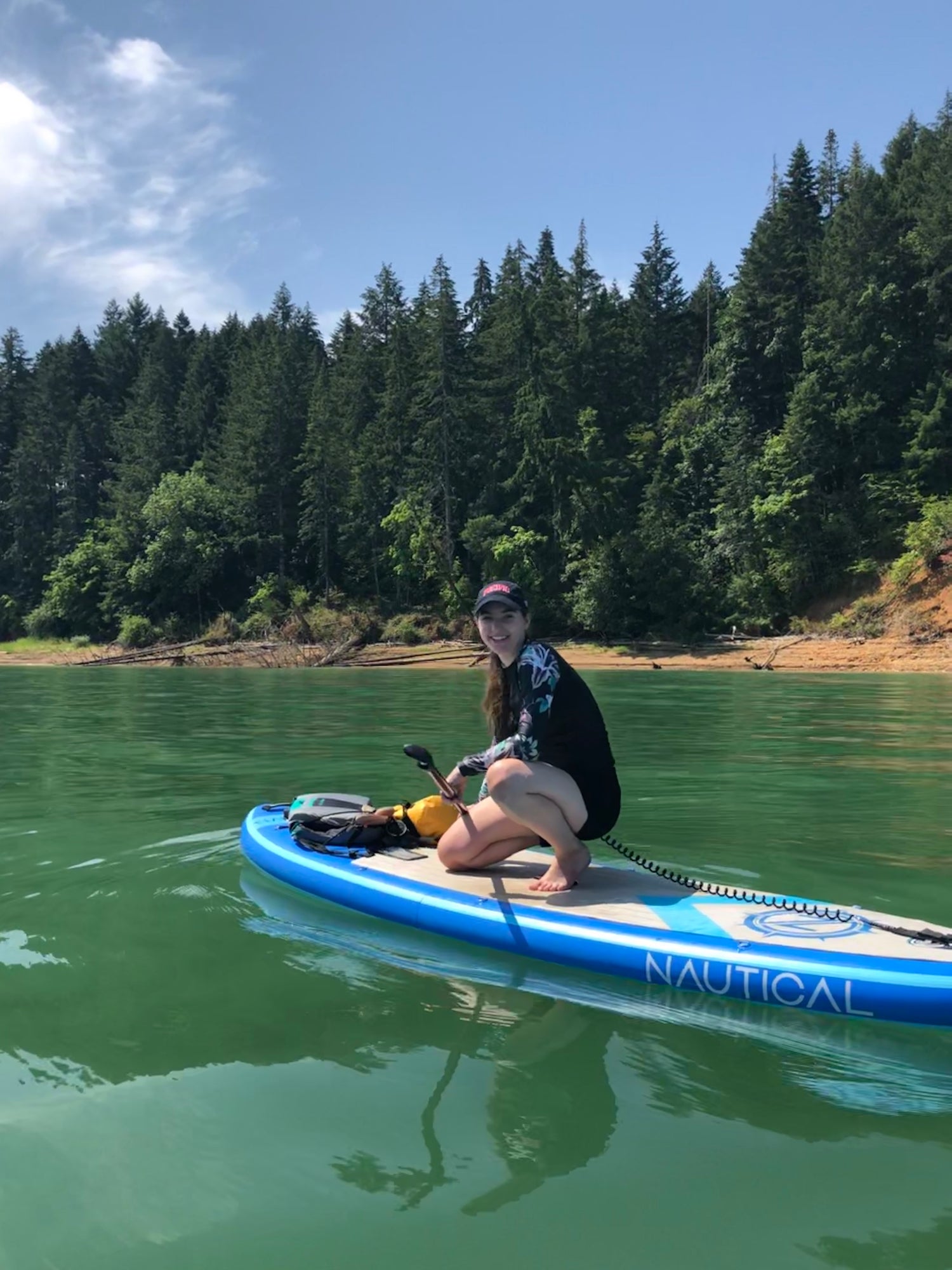 Pintail Paddle Company Founder, Rylee Skidmore, kneeling on her stand up paddle board at the lake.
