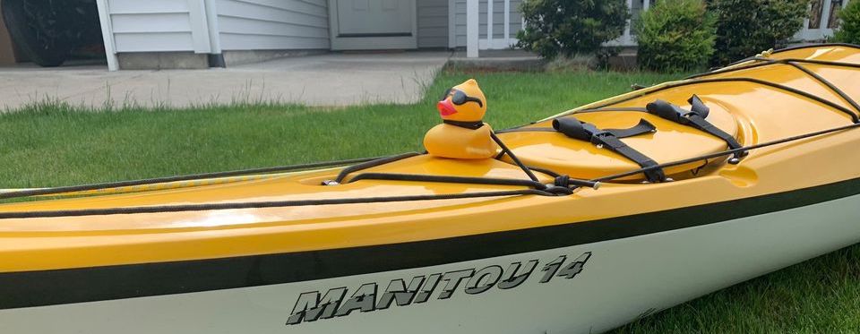 Yellow rubber duck with sunglasses strapped to the front of a kayak.